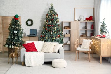 Noel için dekore edilmiş oturma odasının içi kanepe, raf ünitesi ve beyaz tuğla duvarın yanındaki şifoniyerle süslenmiş.