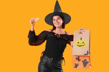 Cadılar Bayramı için giyinmiş genç bir kadın alışveriş torbaları ve sarı arka planda kredi kartı olan bir cadı.