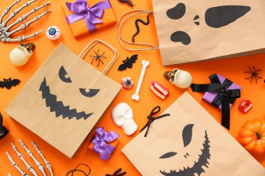 Renkli arkaplanda Cadılar Bayramı için kağıt alışveriş torbaları, hediyeler, süslemeler ve şekerlerle kompozisyon