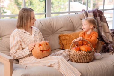 Küçük kızı ve evdeki kanepede oturan Cadılar Bayramı balkabaklarıyla mutlu bir anne.