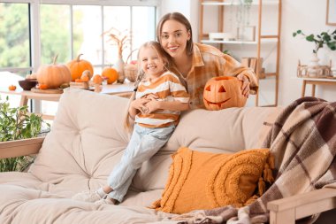 Küçük kızıyla mutlu bir anne ve evdeki kanepede oyulmuş Cadılar Bayramı balkabağı.