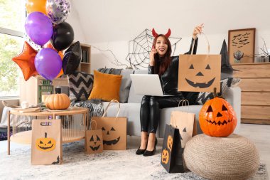 Cadılar Bayramı için giydirilmiş genç Asyalı kadın evde bilgisayar ve çanta alışverişi yapıyor.