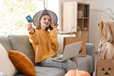 Cadı şapkalı genç bir kadın Cadılar Bayramı için internette kredi kartı alışverişi yapıyor.