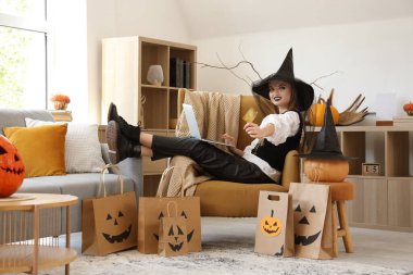 Cadılar Bayramı için giyinmiş genç bir kadın. Kredi kartı ve laptop ile evde online alışveriş yapıyor.