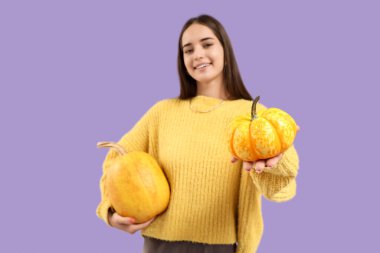 Mor arka planda balkabakları olan güzel, mutlu genç bir kadın.