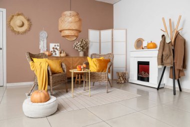 Hasır koltuklu, şömineli ve sonbahar dekorlu şık bir oturma odası.