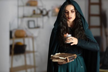 Evinde yanan mum ve büyü kitabı olan genç cadı.