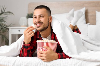 Patlamış mısırlı genç adam yatakta film izliyor.