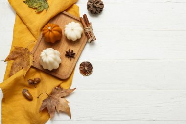 Balkabağı şeklinde mumlar, sonbahar yaprakları ve hafif ahşap arka planda baharatlar.