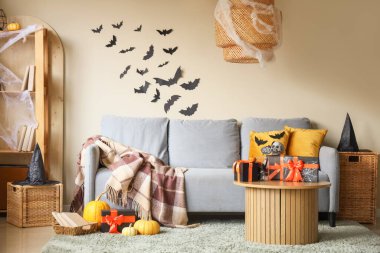 İçinde gri kanepe, Cadılar Bayramı süslemeleri ve hediye kutuları olan şenlikli bir oturma odası.