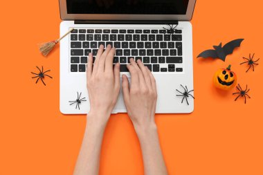 Modern dizüstü bilgisayarlı kadın elleri ve renkli arka planda Cadılar Bayramı için dekorasyonlar