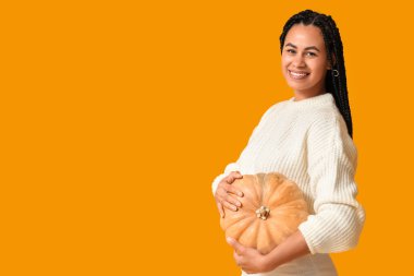 Sarı arka planda büyük bir balkabağı olan güzel, mutlu, Afro-Amerikan kadın.