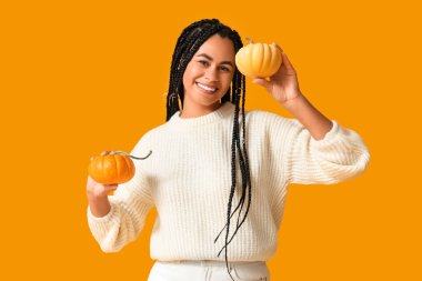 Sarı arka planda balkabakları olan güzel, mutlu, Afro-Amerikan bir kadın.