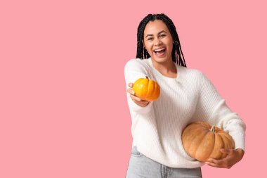 Pembe arka planda turuncu balkabakları olan güzel, mutlu, Afro-Amerikalı bir kadın.