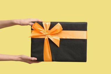 Sarı arka planda Cadılar Bayramı hediye kutusu olan kadın eller.