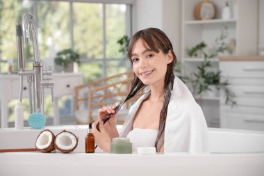 Güzel, genç, mutlu bir kadın evdeki küvette saçına hindistan cevizi yağı sürüyor.