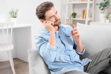 Evdeki kanepede kulak ağrısından muzdarip yakışıklı genç adam.