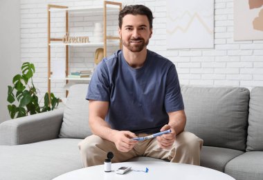 Evde kanepede oturan, elinde tükenmez kalemle şeker hastası genç bir adam.