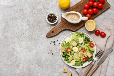 Lezzetli Sezar salatası, limon, biber ve gri arka planda sos teknesi.