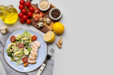 Lezzetli tavuklu Sezar salatası ve gri arka planda malzemeler.