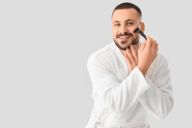 Beyaz arka planda tıraş bıçağı olan bornozlu genç bir adam.