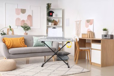 Aydınlık oturma odasının içinde sentezleyici, koltuk ve raf ünitesi var.