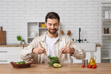 Yakışıklı adam mutfaktaki ahşap masada avokado ve domatesli lezzetli lahana salatası hazırlıyor.