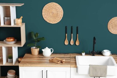 Mutfağın içinde raf ünitesi ve mavi duvarın yanında beyaz tezgahlar var.