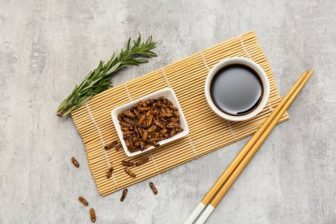 Gri arka planda biberiye ve soya soslu bir kase kızarmış böcek.