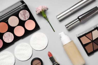 Pamuk yastıklı kompozisyon, kirpik bigudisi, çiçek ve makyaj ürünleri gri arka planda, yakın plan