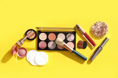 Pamuk yastıklı kompozisyon ve sarı arka planda farklı makyaj ürünleri