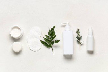 Beyaz arka planda pamuk pedleri, yeşil dallar, kavanozlar ve kozmetik ürünler içeren kompozisyon