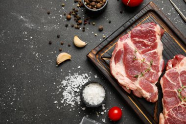 Taze çiğ biftekli ahşap tahta tahta ve siyah arka planda farklı baharatlar.