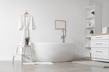 Modern banyoda banyo küvetinin yanındaki sehpanın üzerinde lavanta çiçekleri ve havlu var.