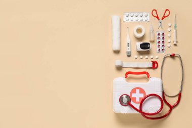 İlk yardım çantası, termometre, tıbbi malzeme ve bej arka planda haplar.