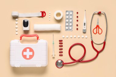 İlk yardım çantalı kompozisyon, tıbbi malzeme ve bej arka planda haplar.