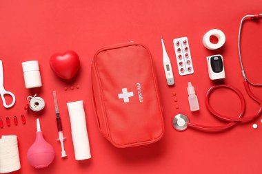 Kırmızı arka planda ilk yardım çantası, haplar ve tıbbi malzemeler var.