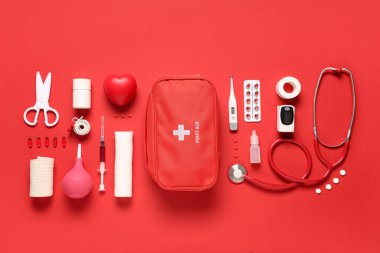 Kırmızı arka planda ilk yardım çantası, haplar ve tıbbi malzemeler var.