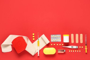 İlk yardım çantası, tıbbi malzemeler ve kırmızı arka planda haplar.