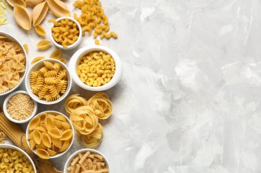 Gri grunge arka planda farklı tipte ham makarna içeren kaseler