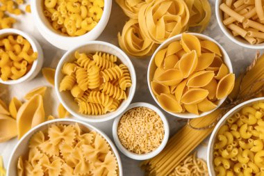 Gri grunge arka planda farklı tipte ham makarna içeren kaseler, yakın plan.