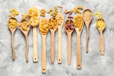 Gri grunge arka planda farklı türde makarna içeren tahta kaşıklar.