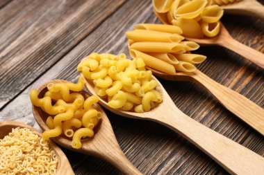 Tahta arka planda farklı türde makarna bulunan tahta kaşıklar, yakın plan.