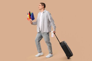 Pasaportu, biletleri, farklı ülkelerin bayrakları ve renkli bir bavulu olan genç bir adam.