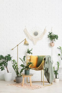 Oturma odasındaki beyaz tuğla duvarın yanında şık koltuğu ve lambası olan farklı bitkiler.
