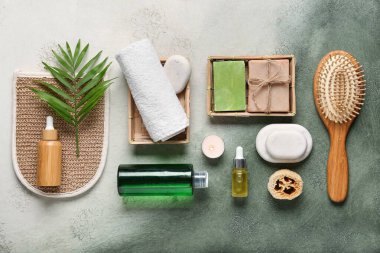 Kozmetik ürünleri şişeleri, banyo aksesuarları ve yeşil grunge arka planda spa taşlarıyla kompozisyon