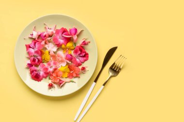 Farklı güzel, yenilebilir çiçekli tabaklar ve sarı arka planda çatal bıçak takımı.
