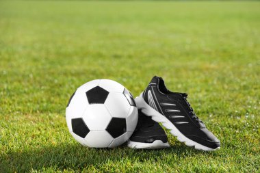 Yeşil stadyum çimlerinde futbol topu ve spor ayakkabıları