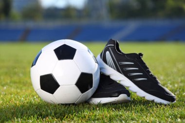 Yeşil stadyum çimlerinde futbol topu ve spor ayakkabıları