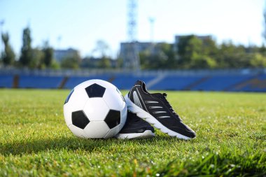 Yeşil stadyum çimlerinde futbol topu ve spor ayakkabıları